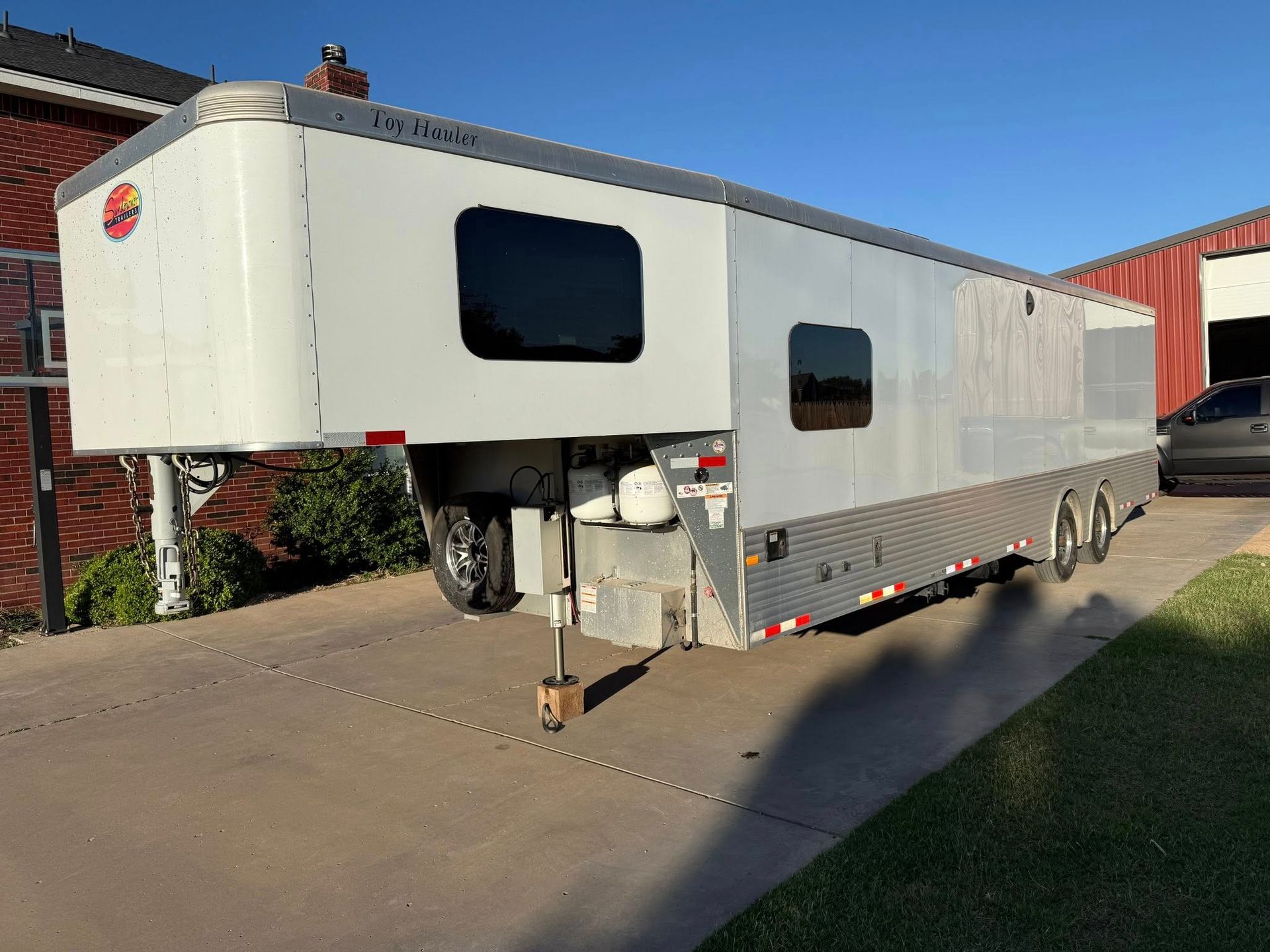 A white trailer is parked in a driveway next to a brick building.