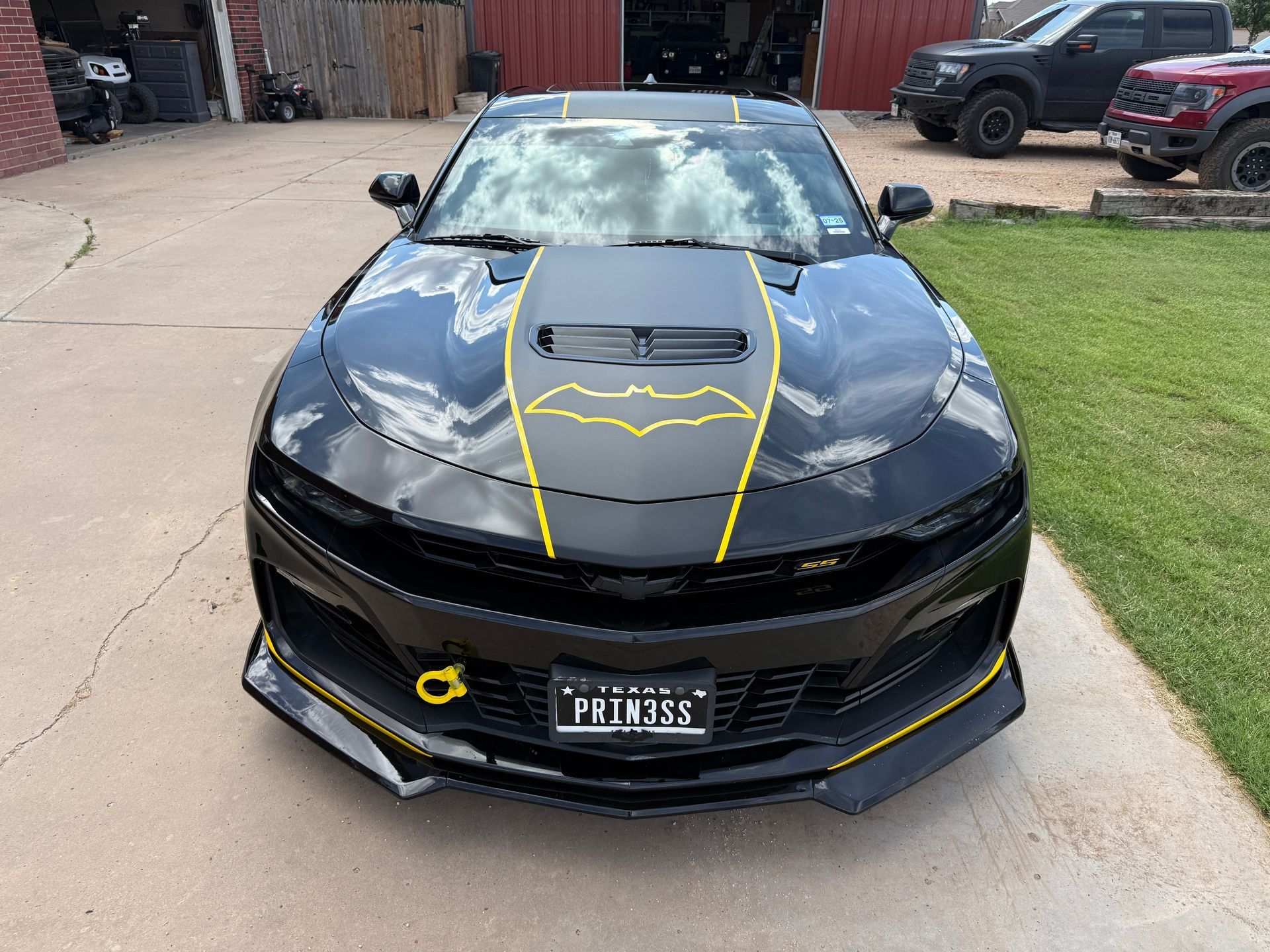 Black Chevrolet Camaro with yellow accents and a Batman-themed hood graphic parked in a driveway.
