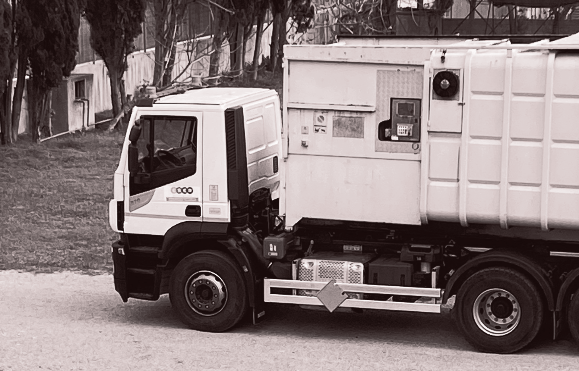 Vista laterale in bianco e nero di un camion della spazzatura bianco parcheggiato su una strada.