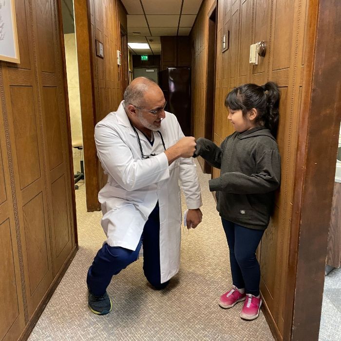Un médico con bata blanca choca el puño con una joven en el pasillo.
