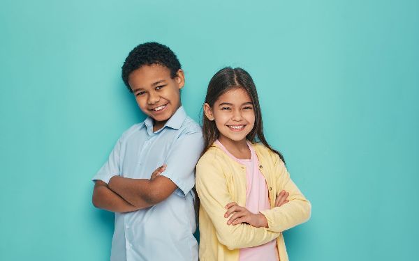 A boy and a girl are standing back to back with their arms crossed.