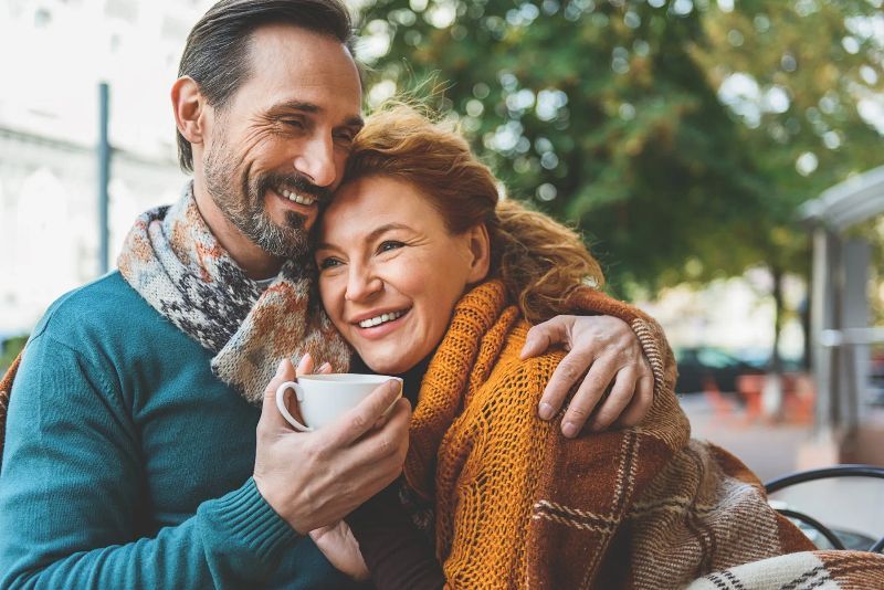 A man is hugging a woman while holding a cup of coffee.