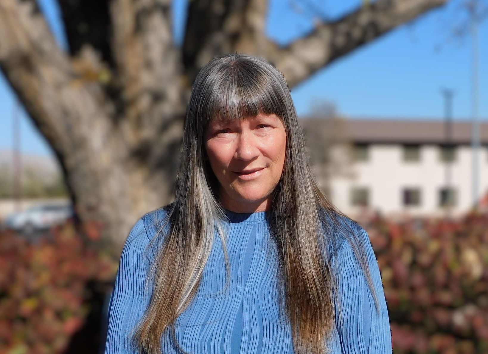 A woman in a blue sweater is standing in front of a tree.