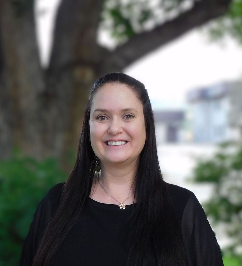 A woman in a black shirt is smiling in front of a tree.