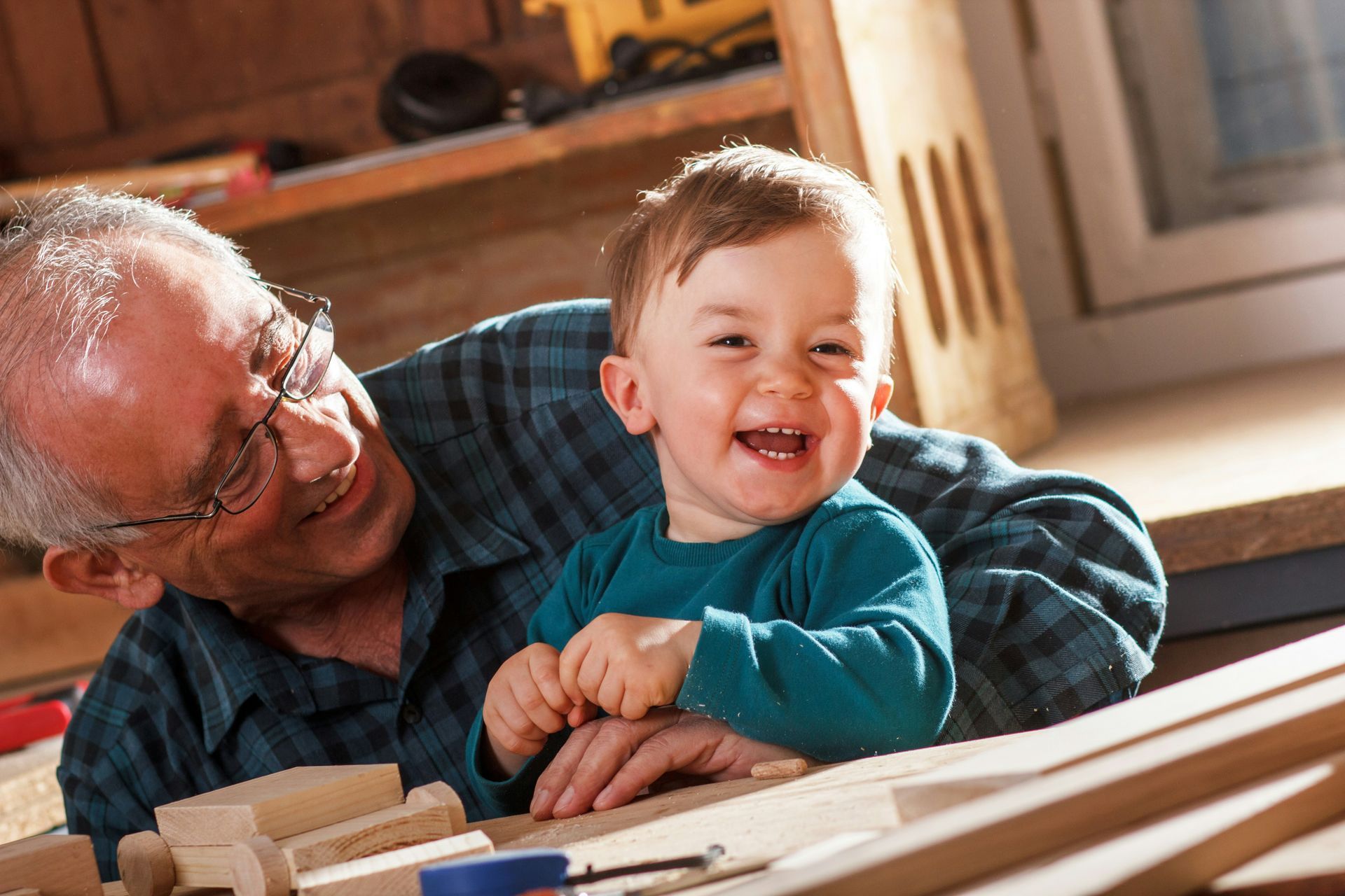 A man is holding a baby in his arms while they play with wood.