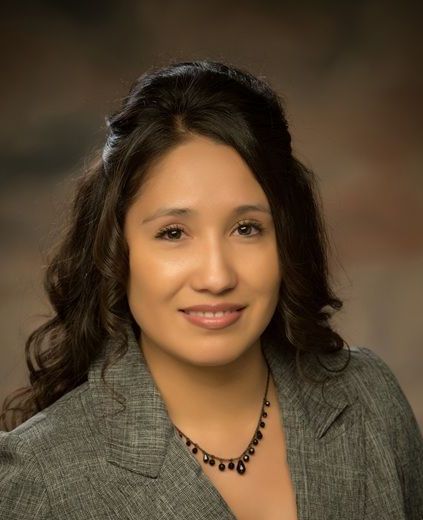 A woman in a suit and necklace is smiling for the camera.