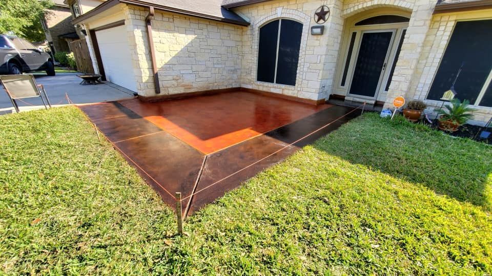 Brown and red stained concrete patio with decorative border in front of a house.