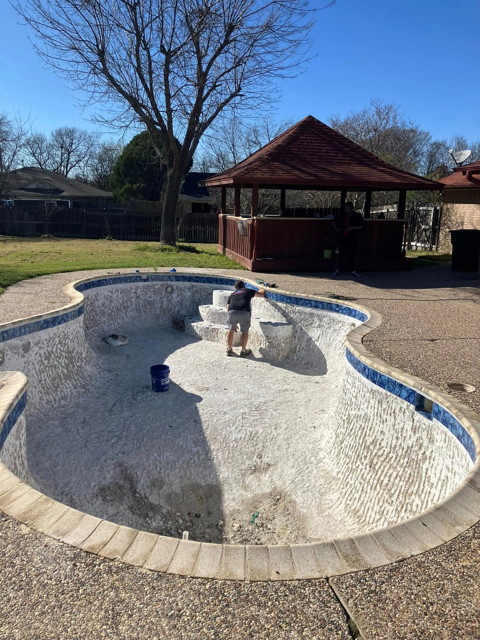 Empty concrete fountain basin in a park, with a red gazebo and bare trees in the background