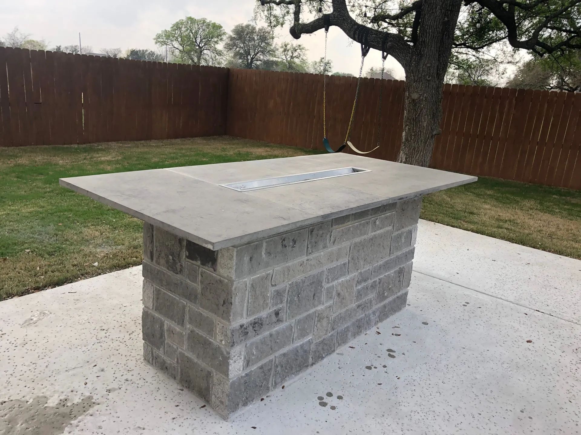 Outdoor stone picnic table on a concrete patio in a fenced backyard