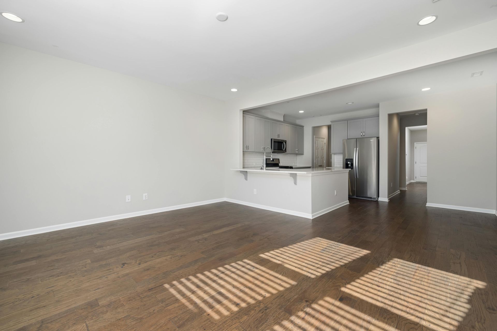 Empty living room with dark wood floor, light gray walls, and open kitchen area.