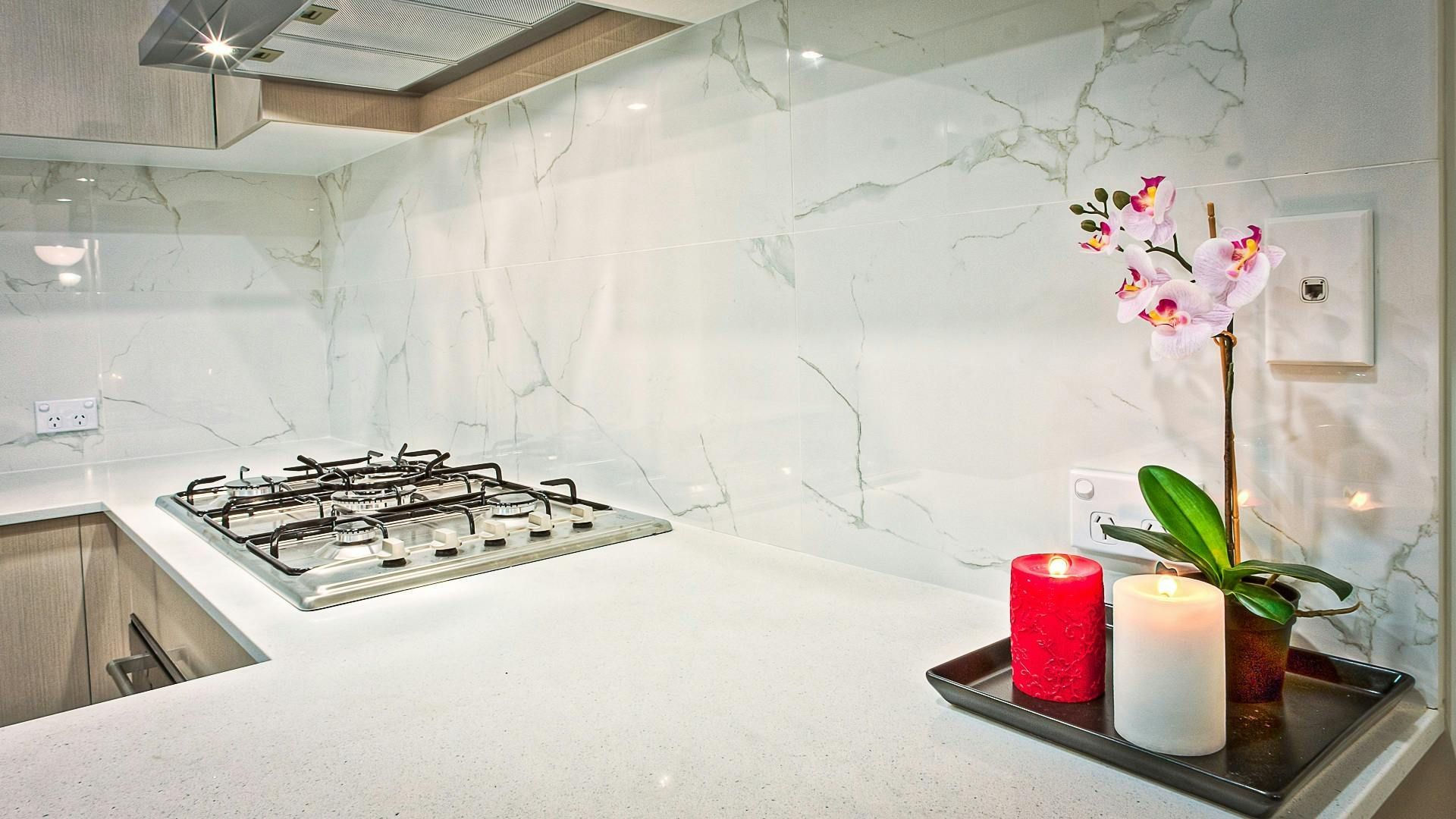 Kitchen with white marble backsplash, stovetop, candles, and orchid on a tray.