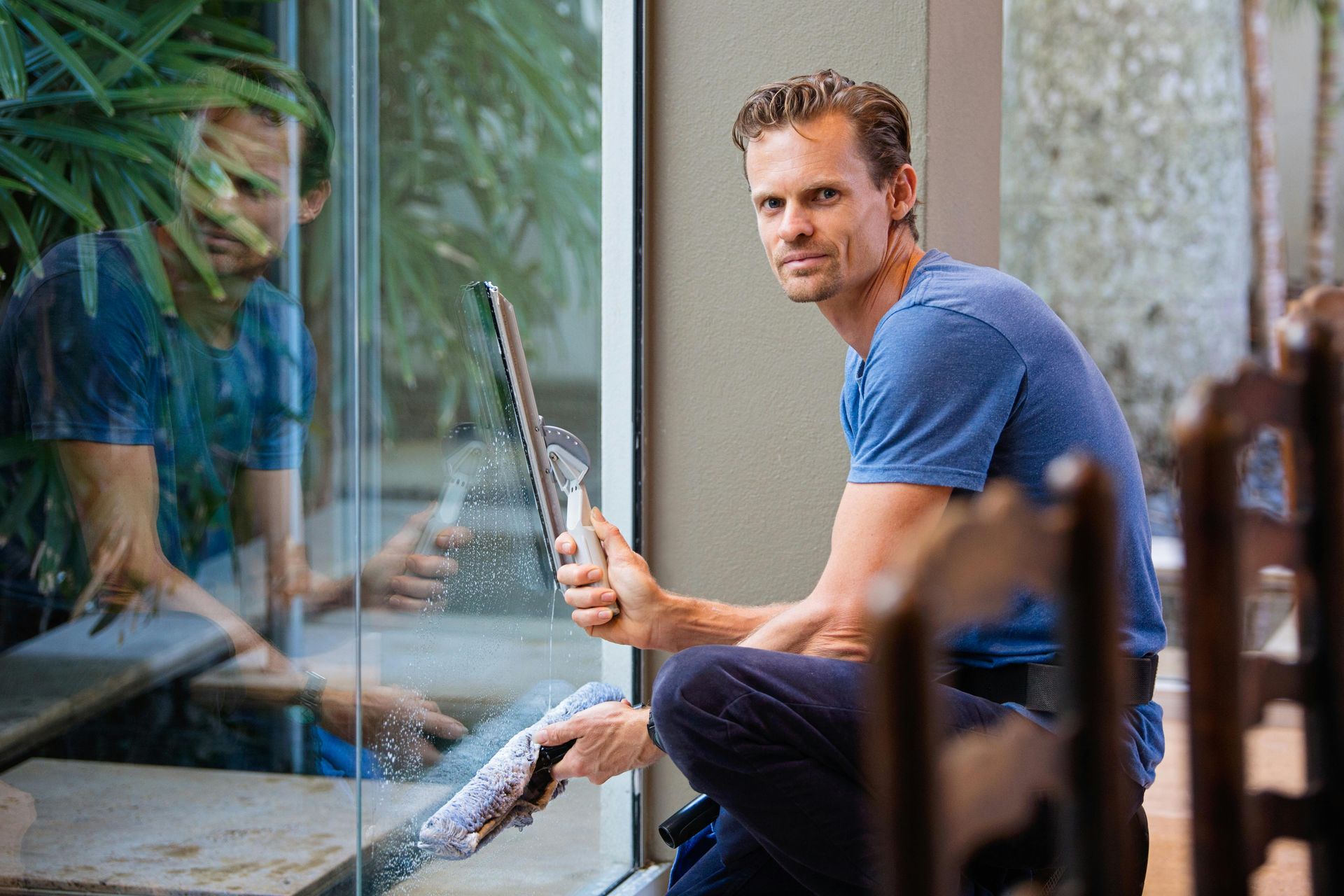 Man cleaning a window with a squeegee, smiling indoors.