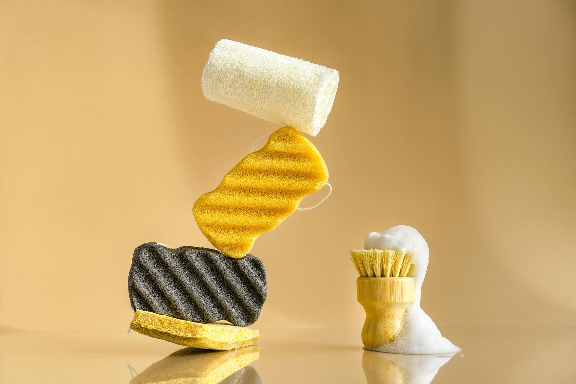 Stack of cleaning sponges and a brush with foam on a neutral background.
