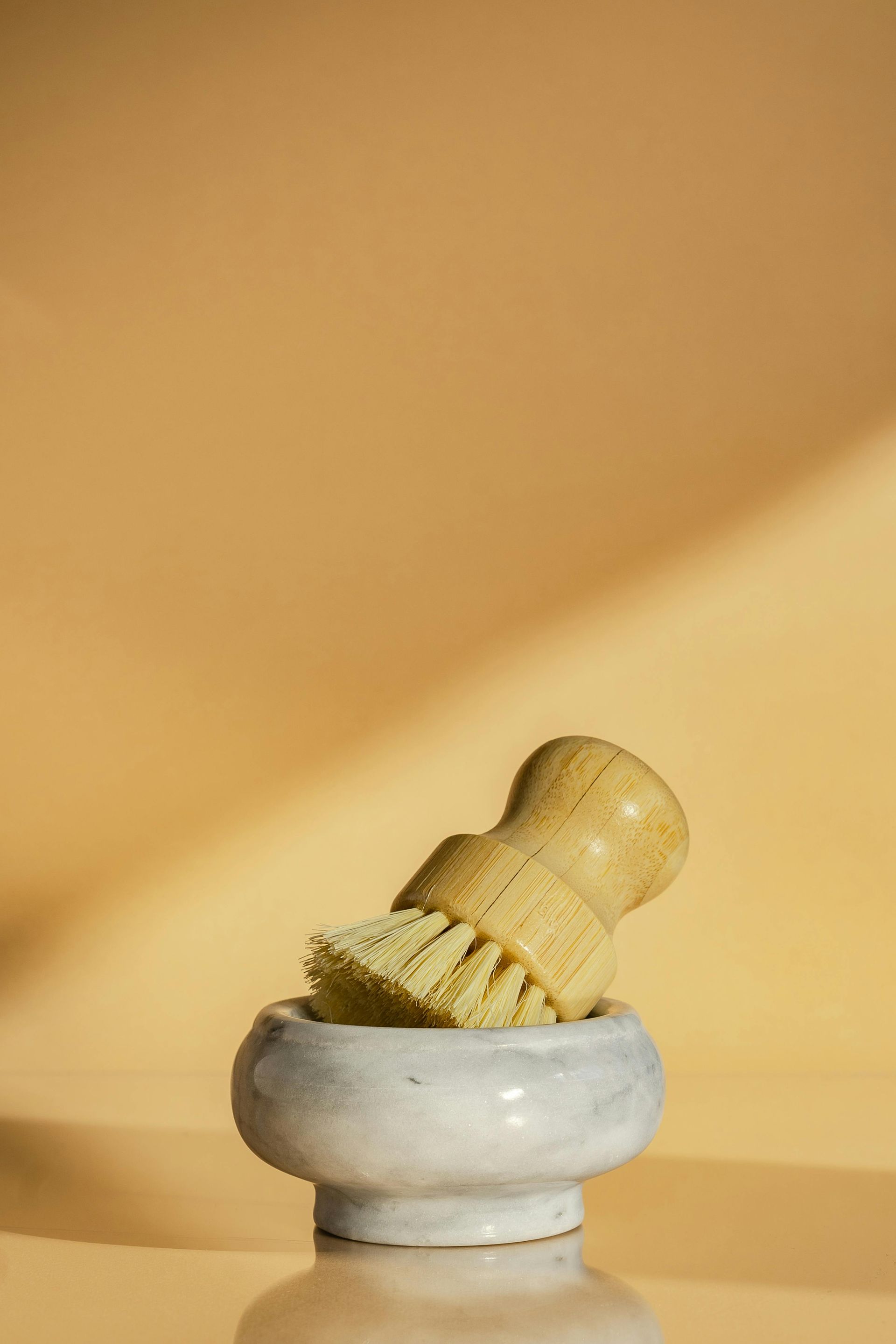 Wooden handled brush in a ceramic bowl, against a yellow background.