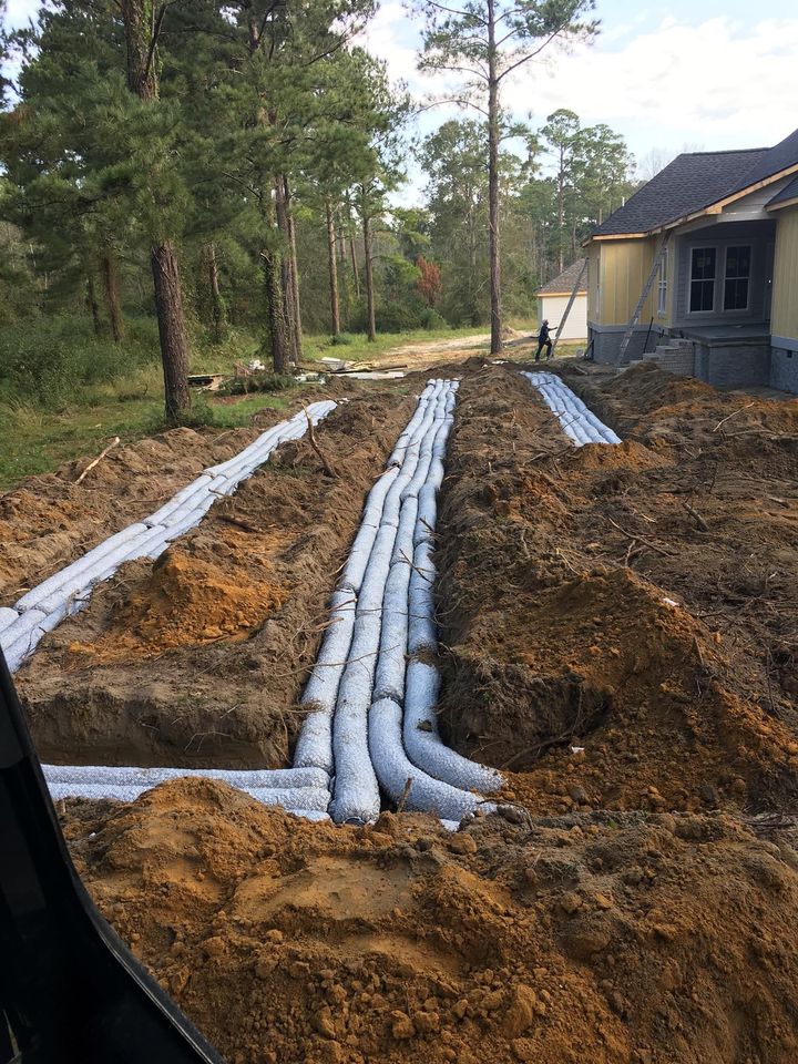 Trenches with white wrapped pipes for drainage near a house under construction.