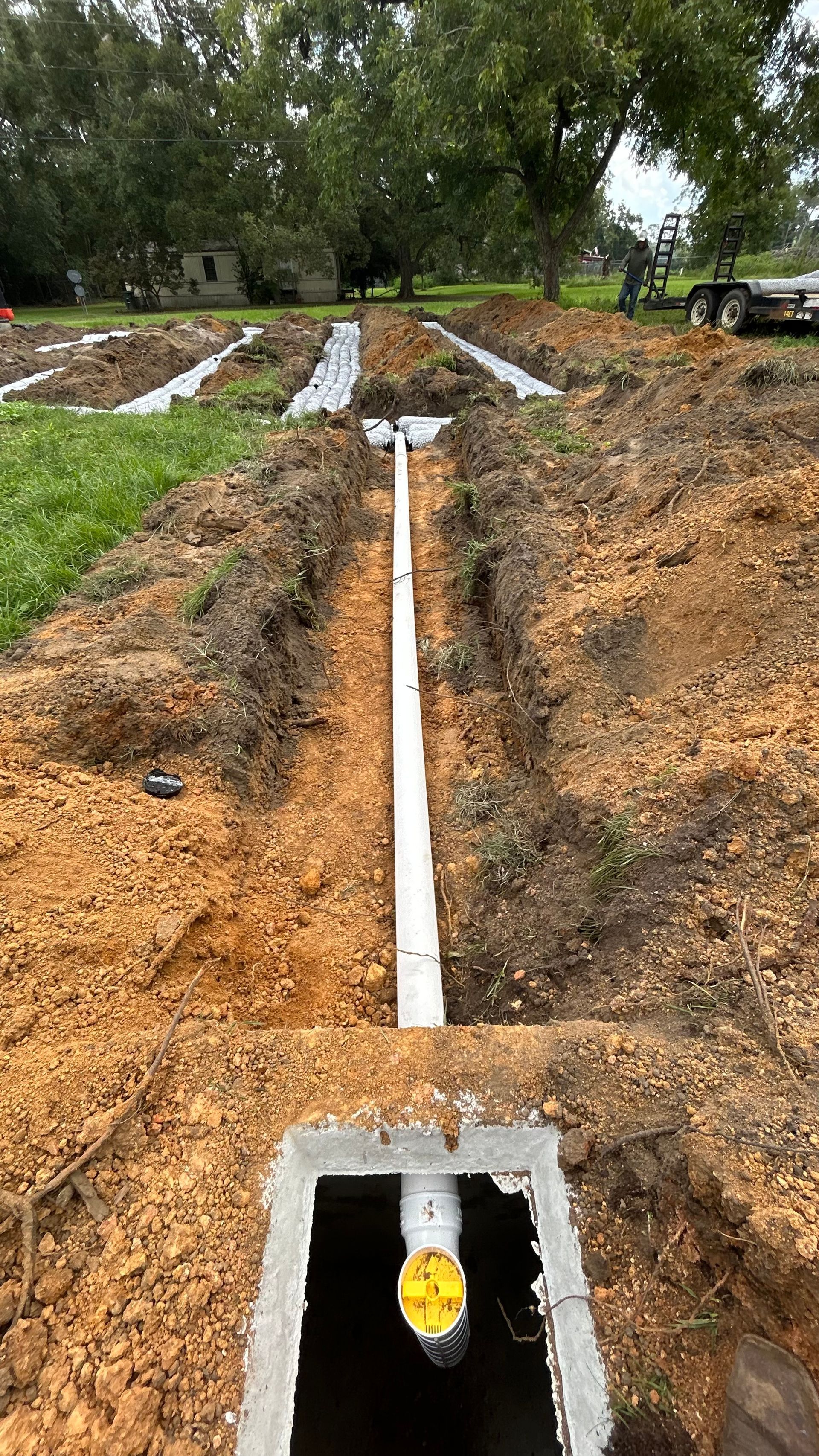 Outdoor trench with white pipe line leading to a concrete utility box in a muddy field