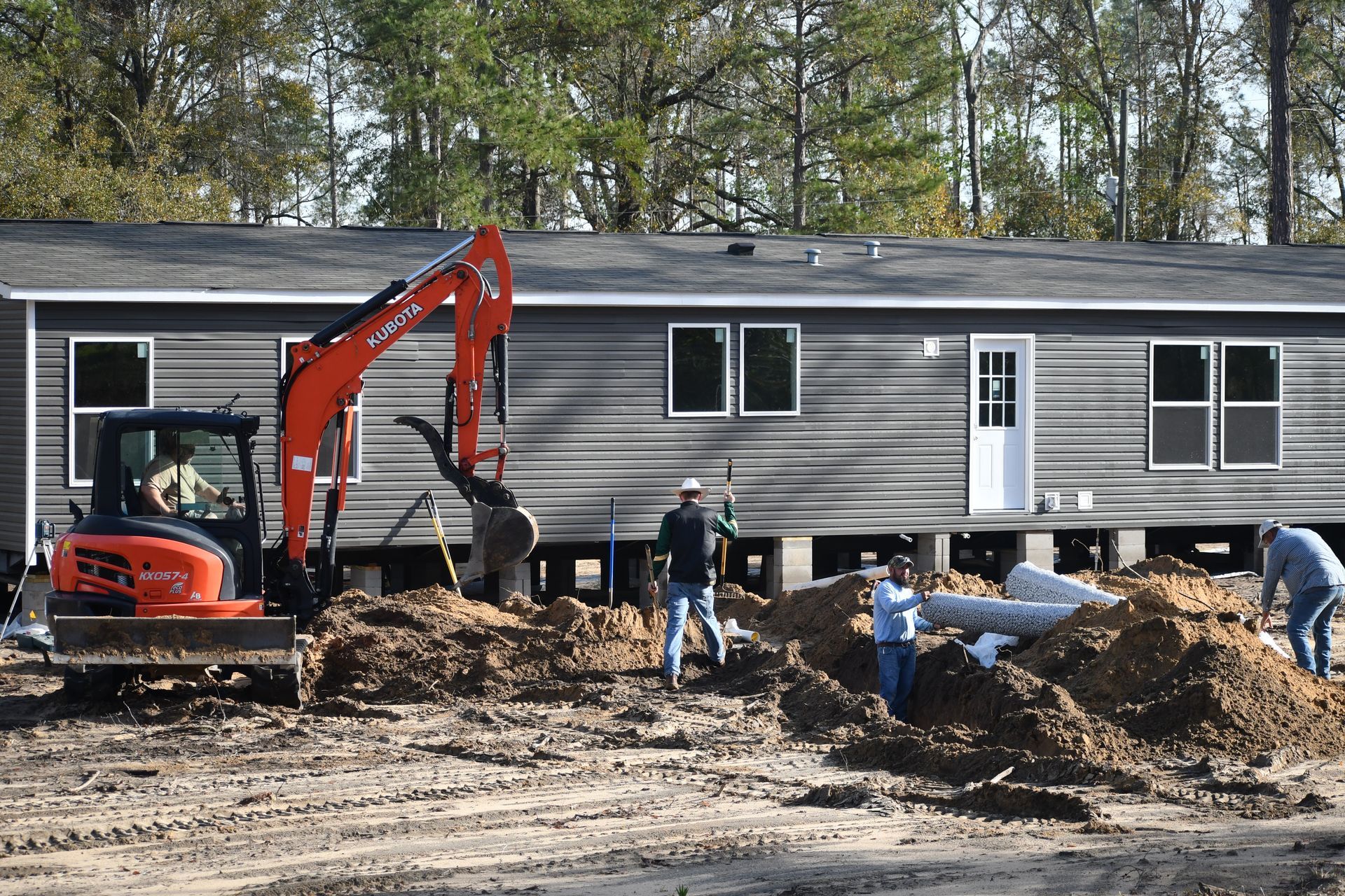 Construction crew installing a modular home with an orange excavator and dirt piles in front.