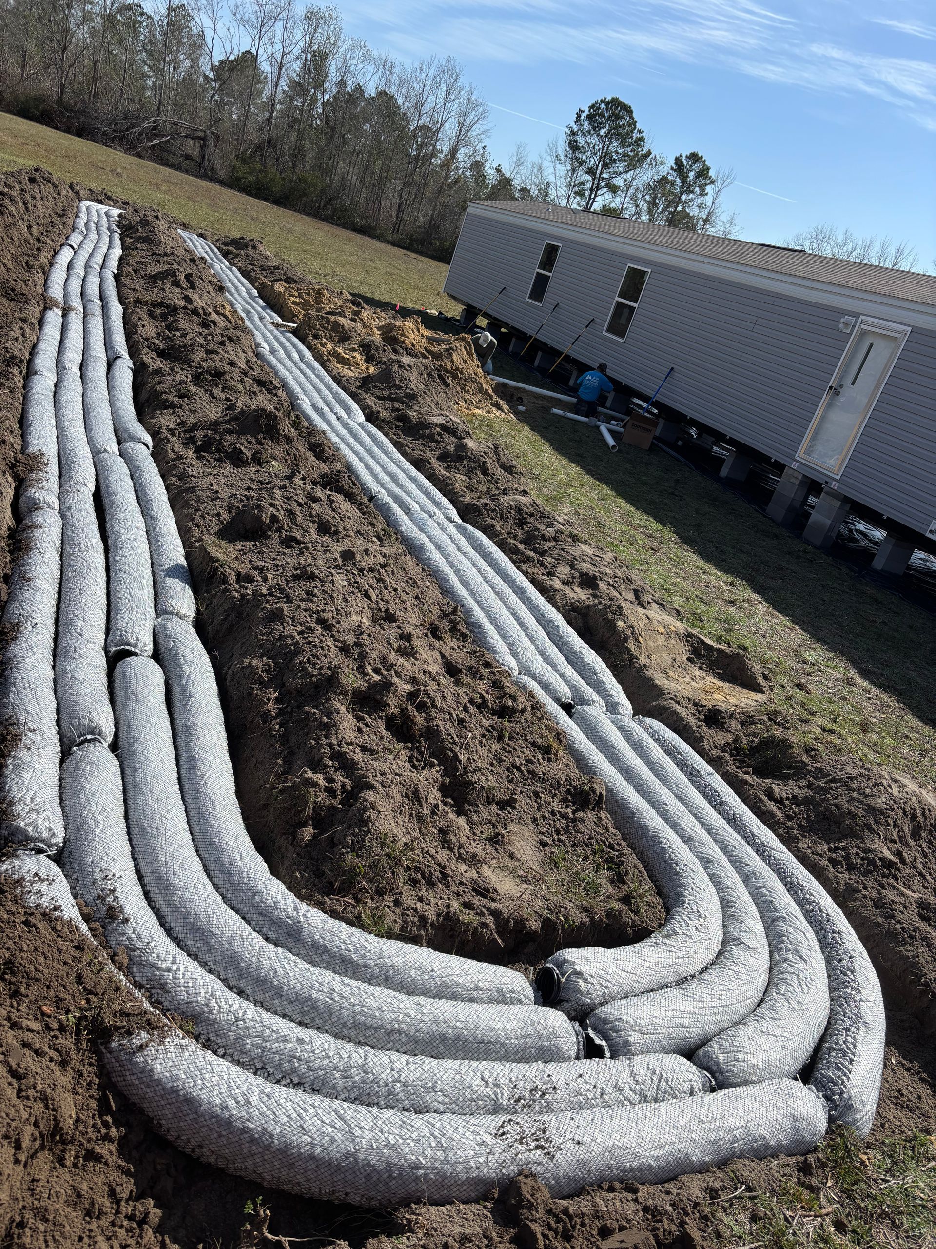 Coiled white hoses laid on a dirt slope beside a metal utility trailer and trees.