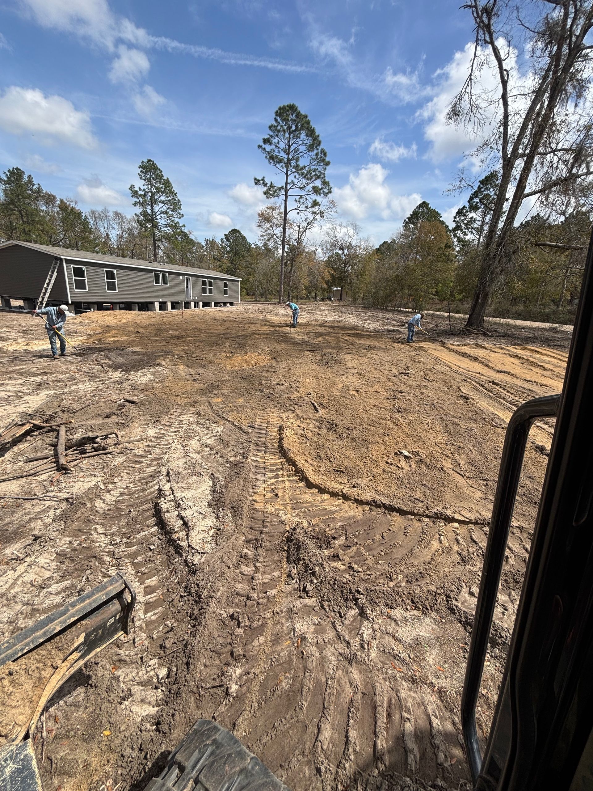 Dirt road construction site with muddy tracks, workers, and trees under a blue sky