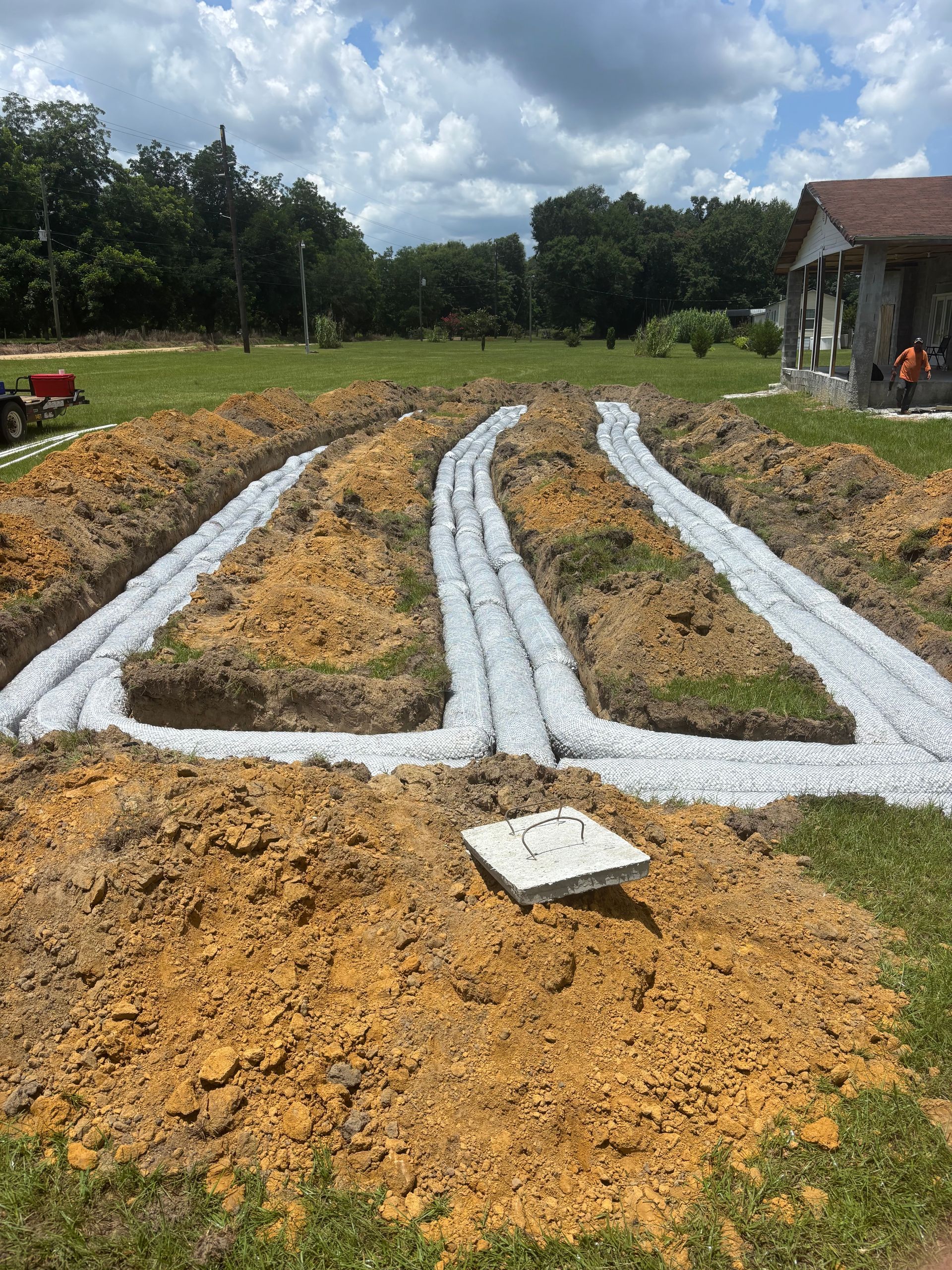 Raised garden beds lined with white plastic mulch in a muddy field beside a small house.