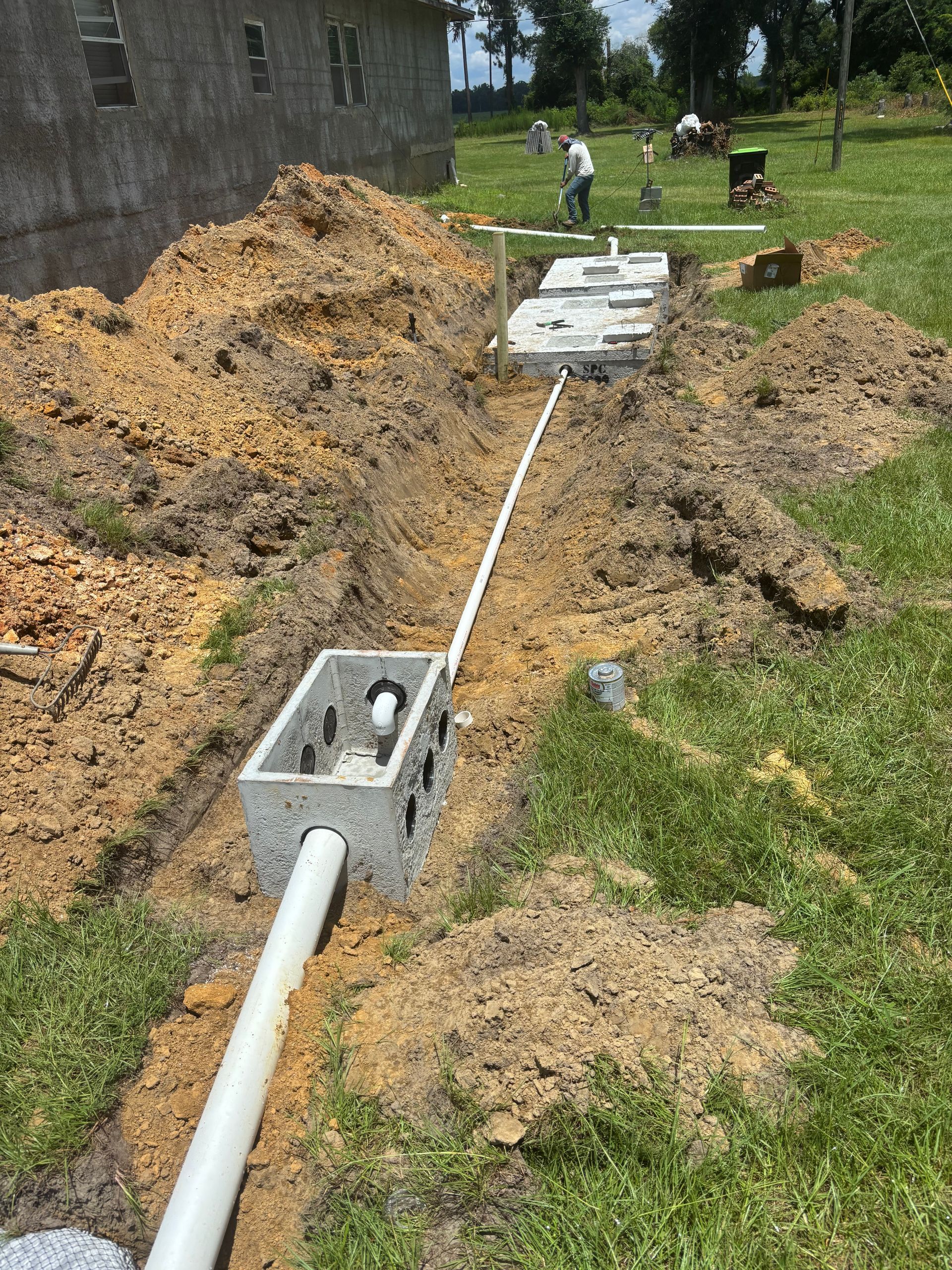 Trenched PVC pipe installed beside a house, with concrete boxes and mounds of excavated soil.