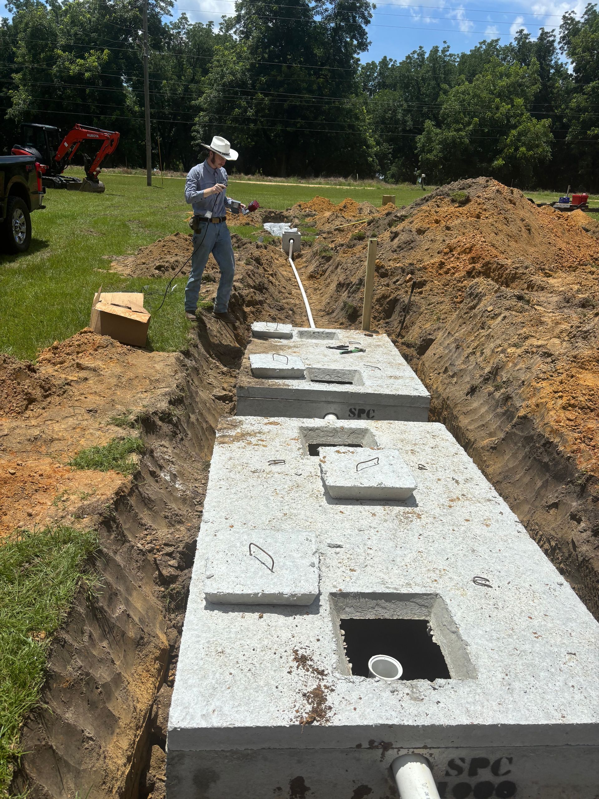Worker standing beside a concrete septic tank trench at an outdoor construction site