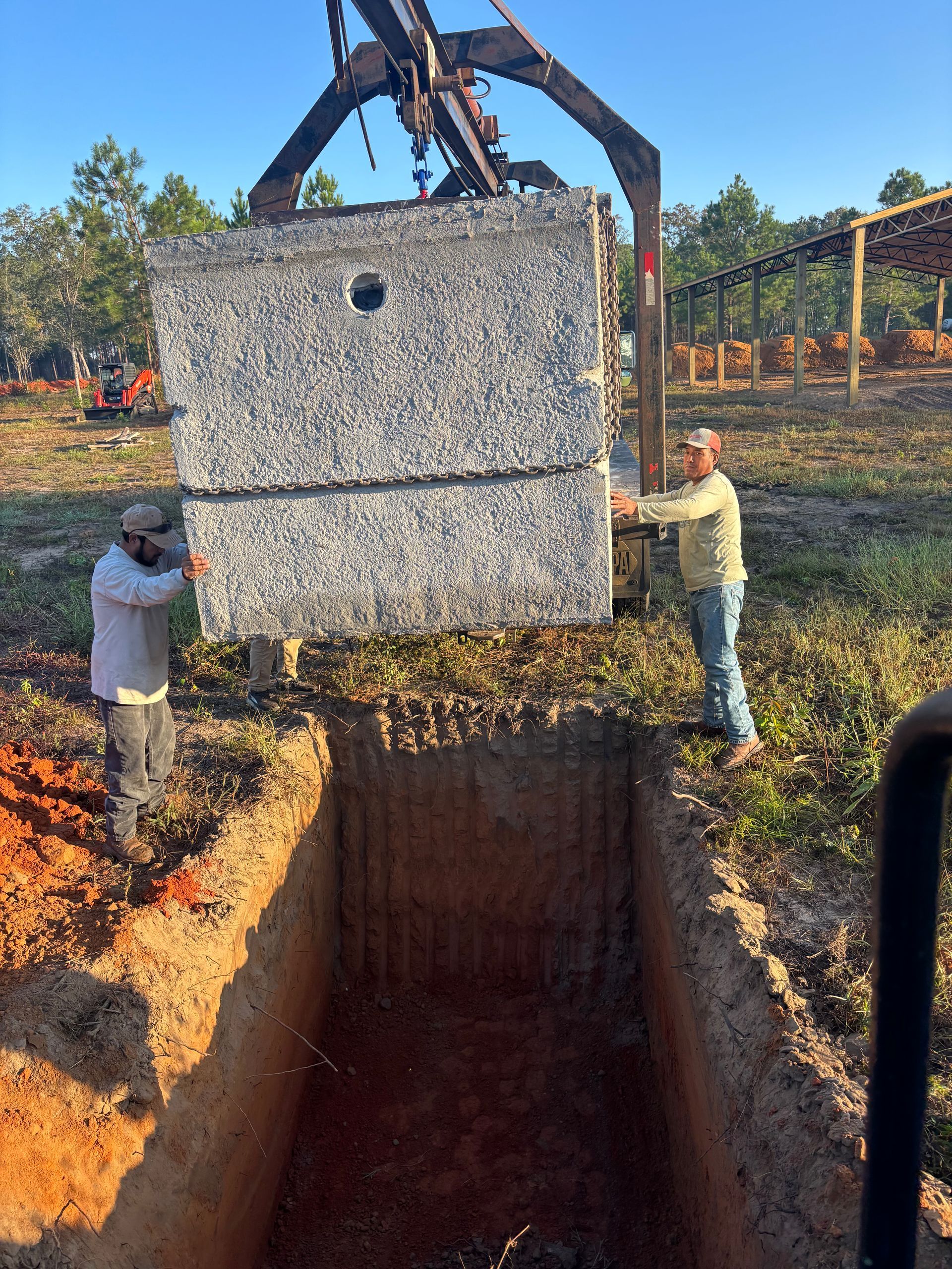 Workers lowering a concrete block into a deep pit with an excavator at a construction site