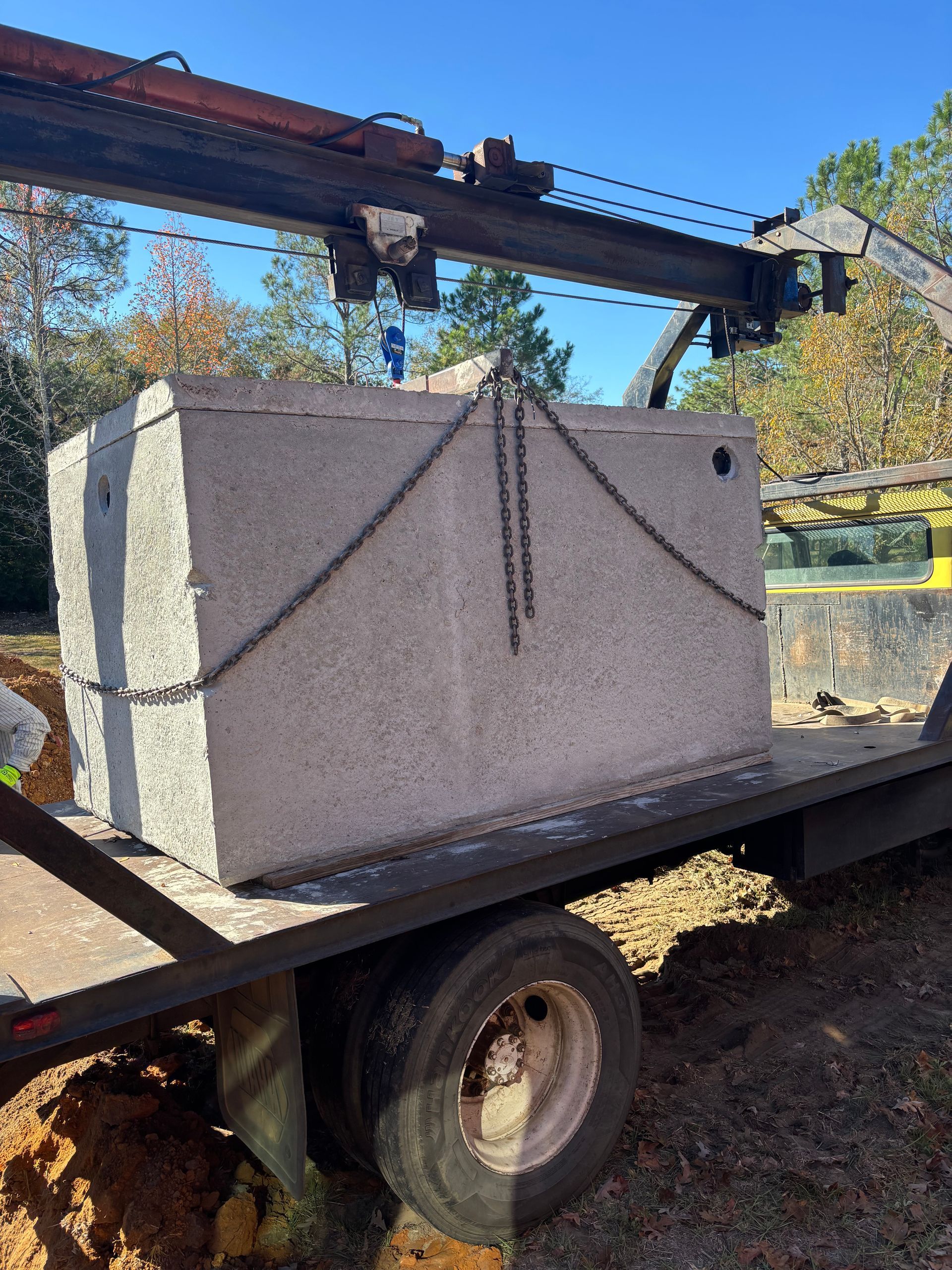 Large gray stone block strapped to a trailer outdoors under a bridge on a sunny day