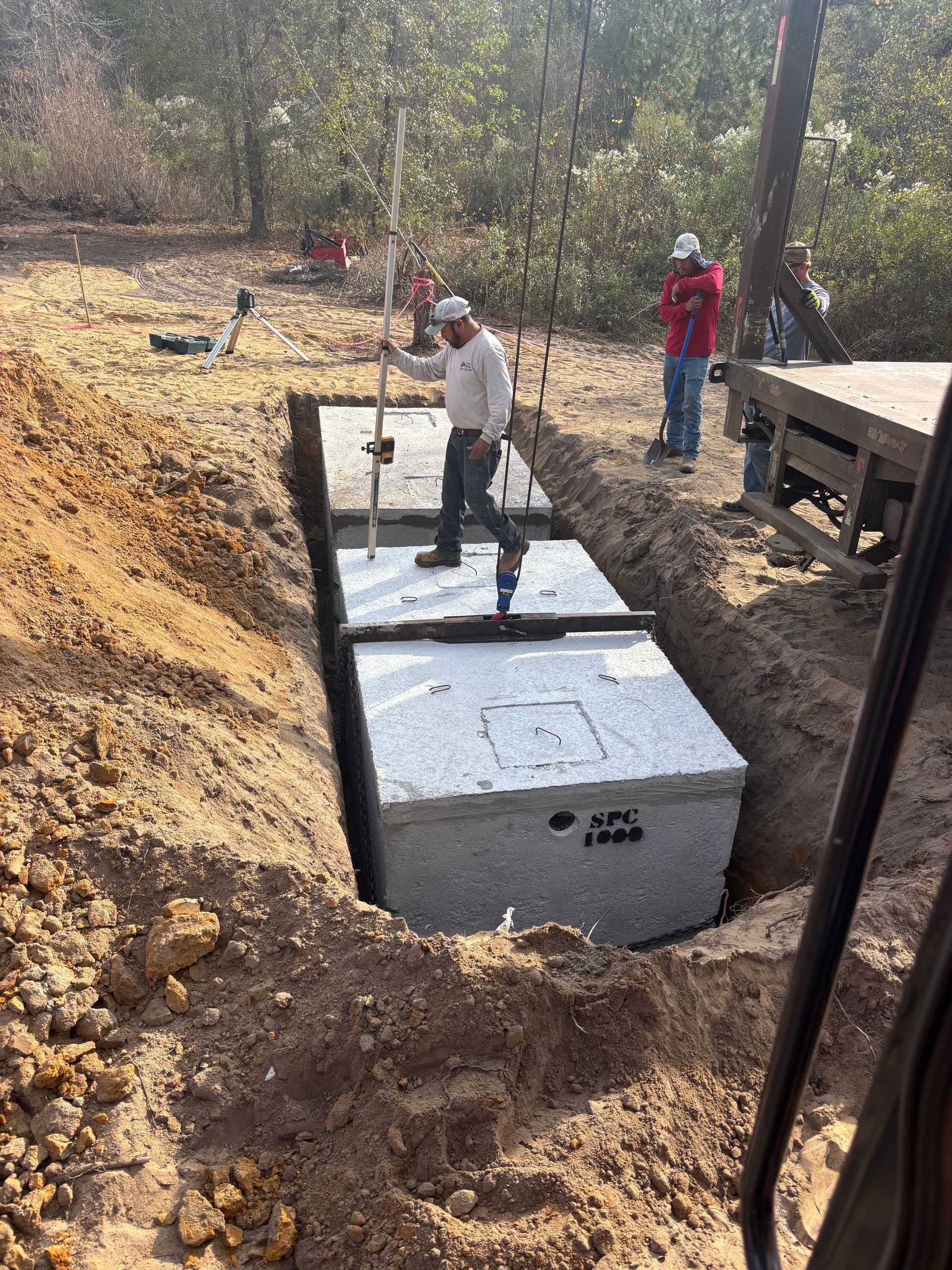 Workers installing large concrete tanks in a dirt excavation site outdoors