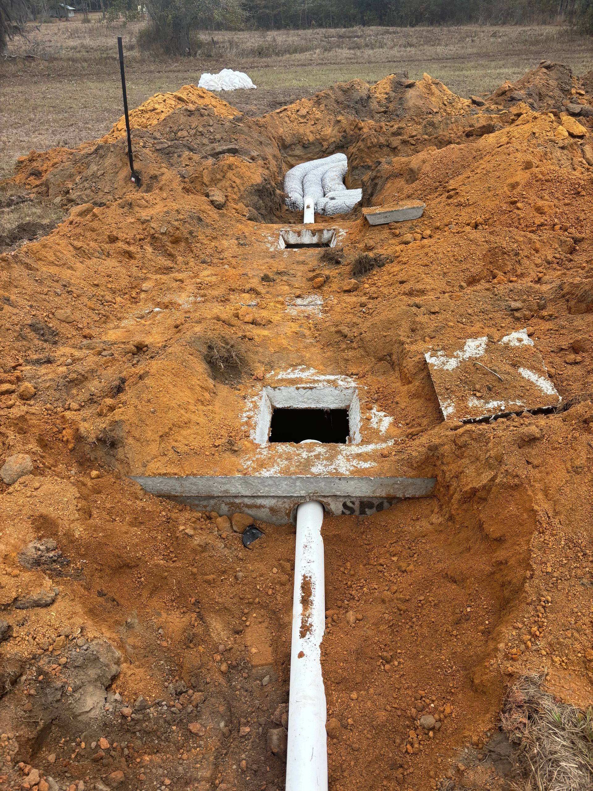 White pipe and black outlet in orange dirt trench at a construction site