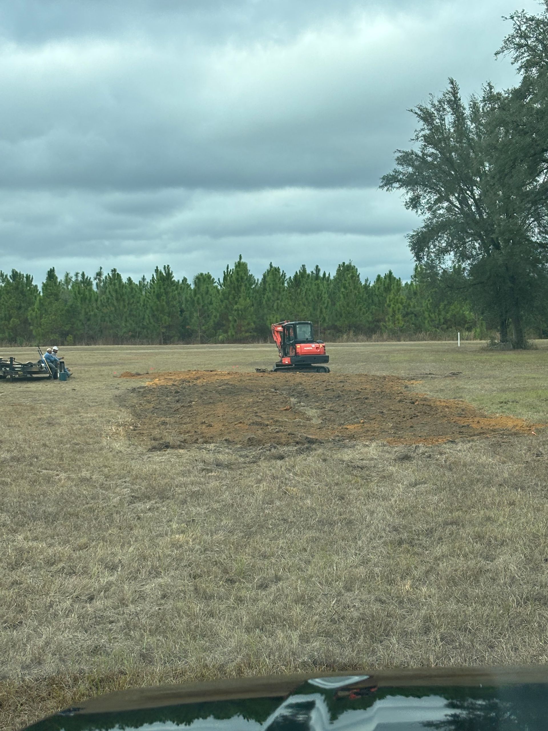 Orange tractor in a field under cloudy skies, with a tree line in the background.