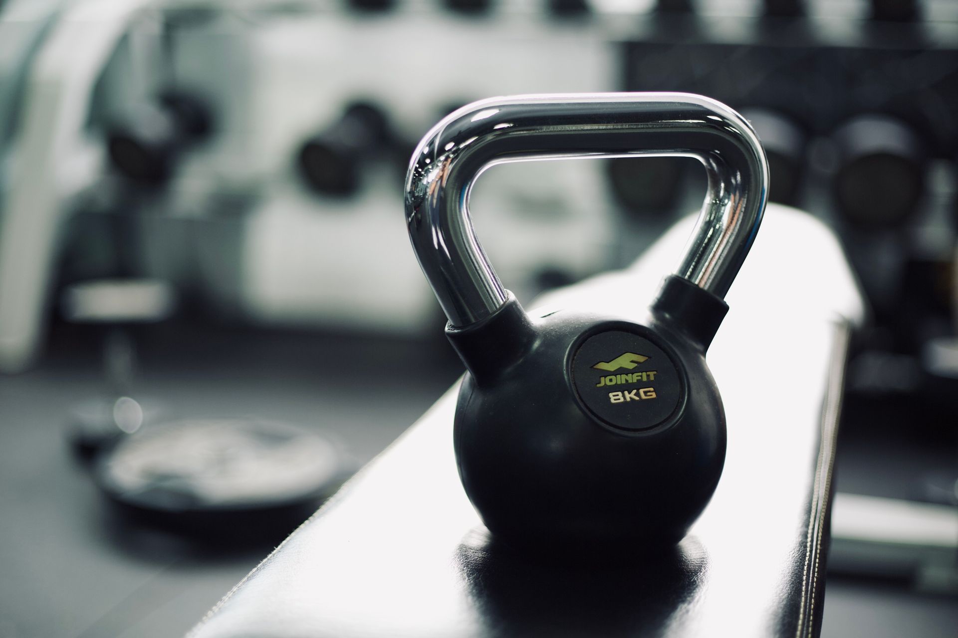 Black kettlebell on a gym bench with blurred workout equipment in the background