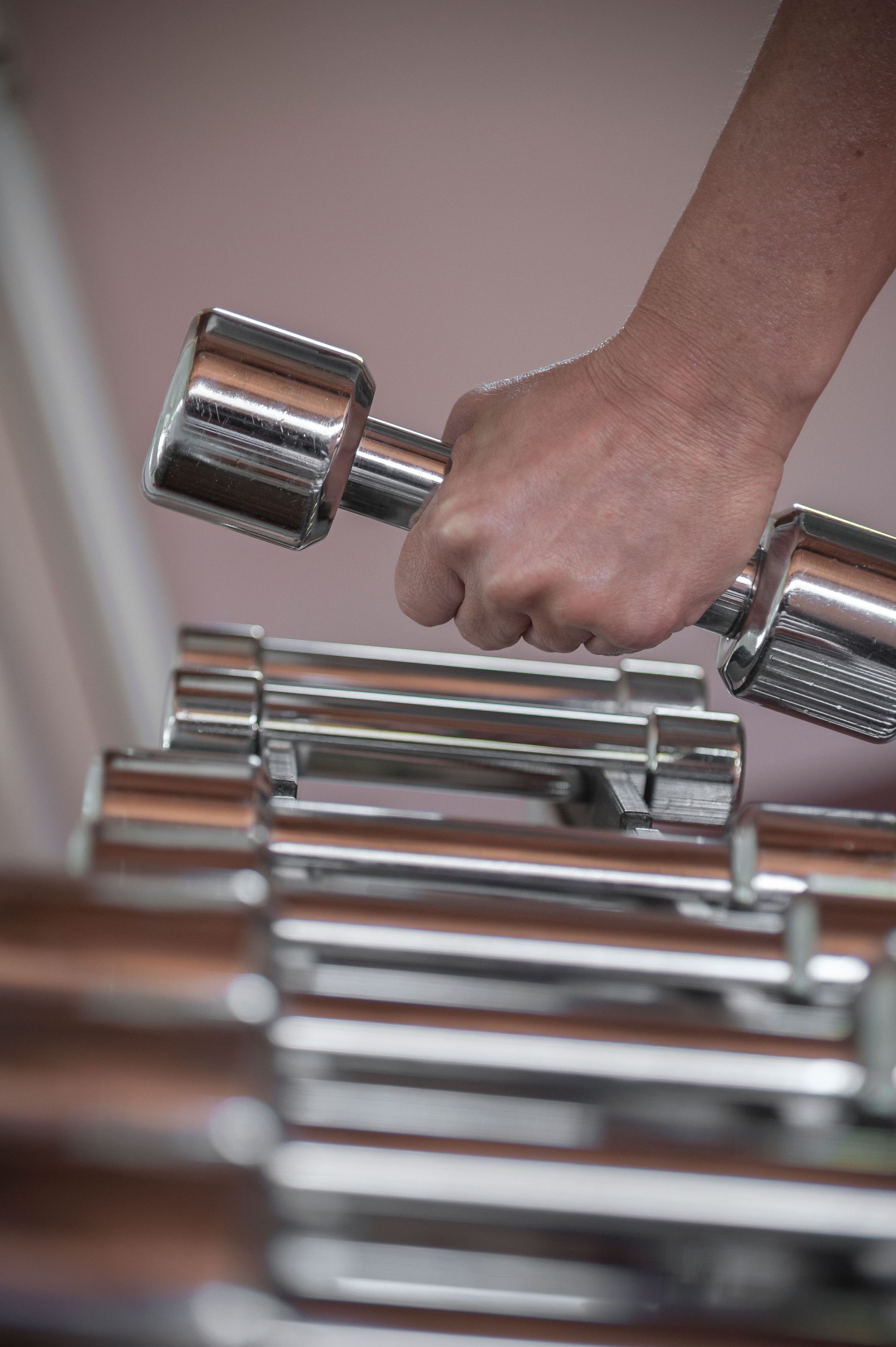 Hand gripping a dumbbell above a rack of chrome weights in a gym