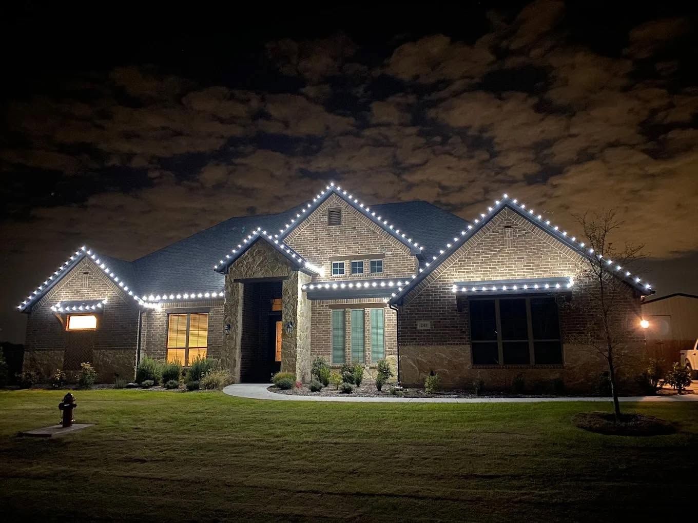 Single-story house at night with white roof lights and a lit front door and windows