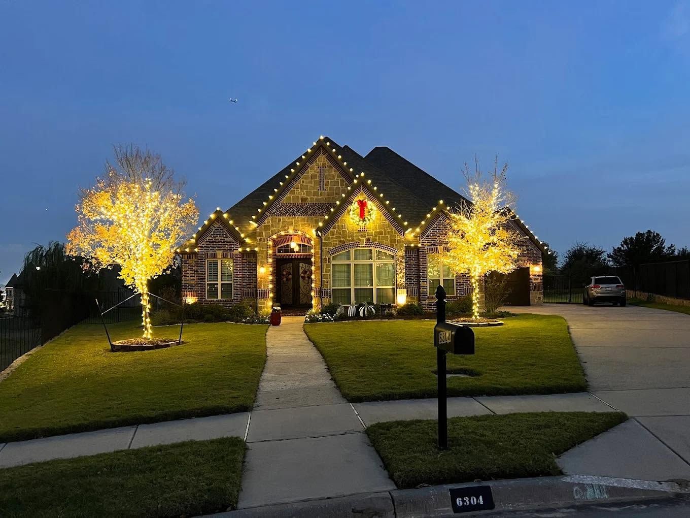 House lit with holiday lights at dusk, with illuminated trees and a front walkway leading to the entrance.