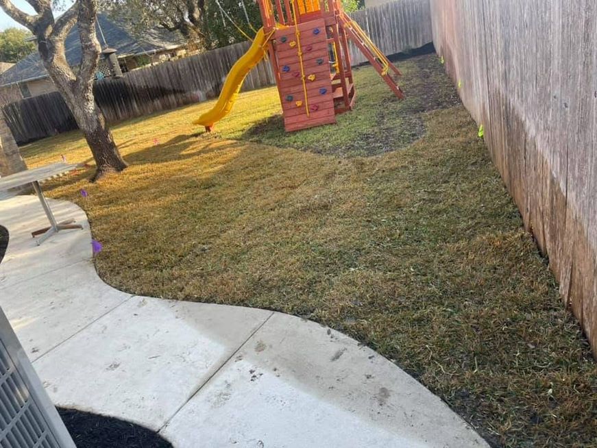 Backyard play area with a yellow slide, red climbing frame, grass, and a curved concrete patio