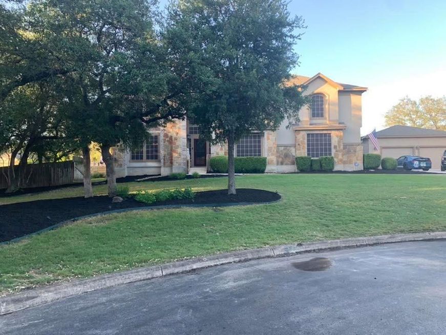 Suburban house with stone exterior, large tree, green lawn, and driveway at dusk