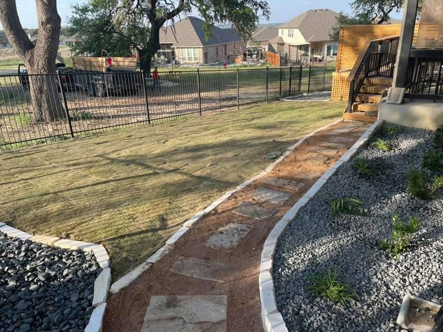 Backyard walkway with fresh concrete borders, gravel edging, lawn, fence, and neighboring houses in the distance