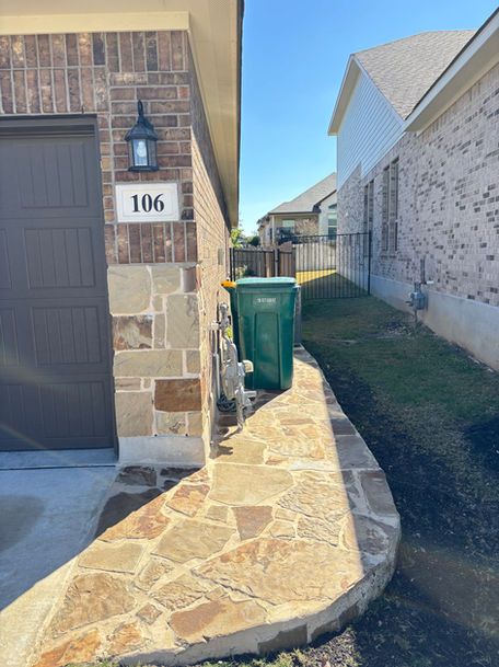 Narrow stone walkway beside house number 106, with a green trash bin and side yard between homes
