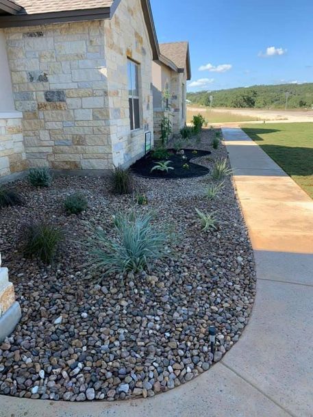 Front yard landscaping with rocks, succulents, and a concrete walkway beside a stone house