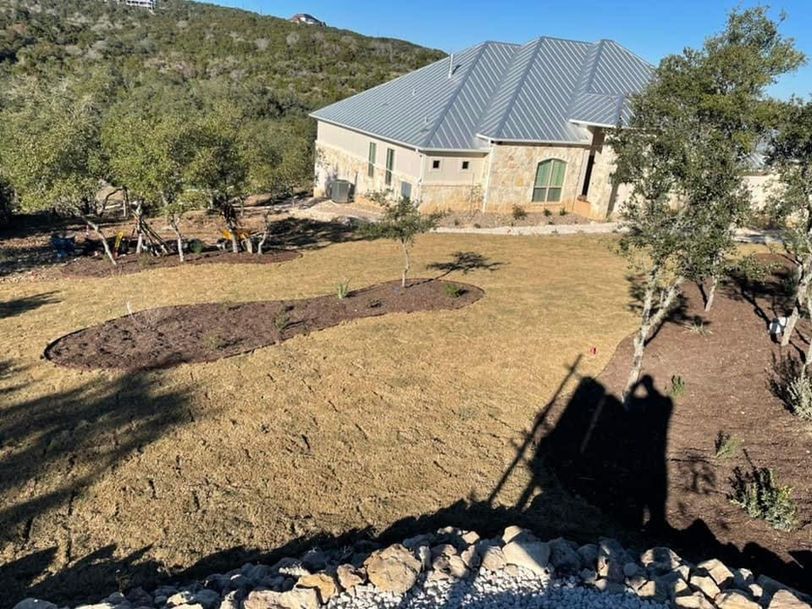 House with gray roof in a dry landscaped yard, surrounded by trees and hillside greenery.