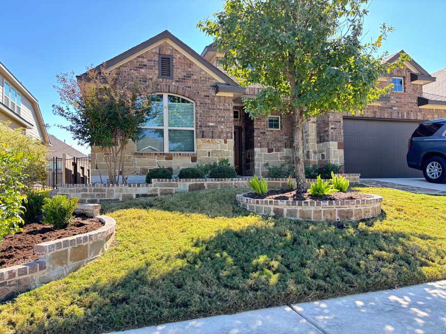 Brick suburban house with front yard, curved stone flower beds, and a parked black SUV.