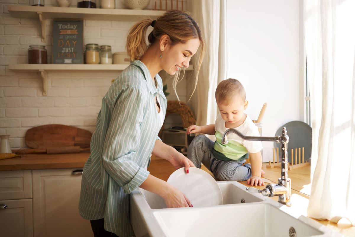A woman and a child are washing dishes in a kitchen sink.