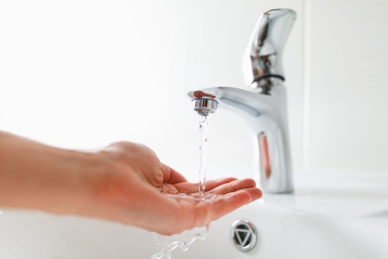 A person is washing their hands under a faucet in a bathroom.