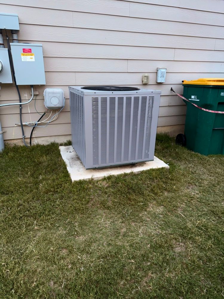 Outdoor air conditioner unit on a wall, surrounded by green vines and pink flowers.