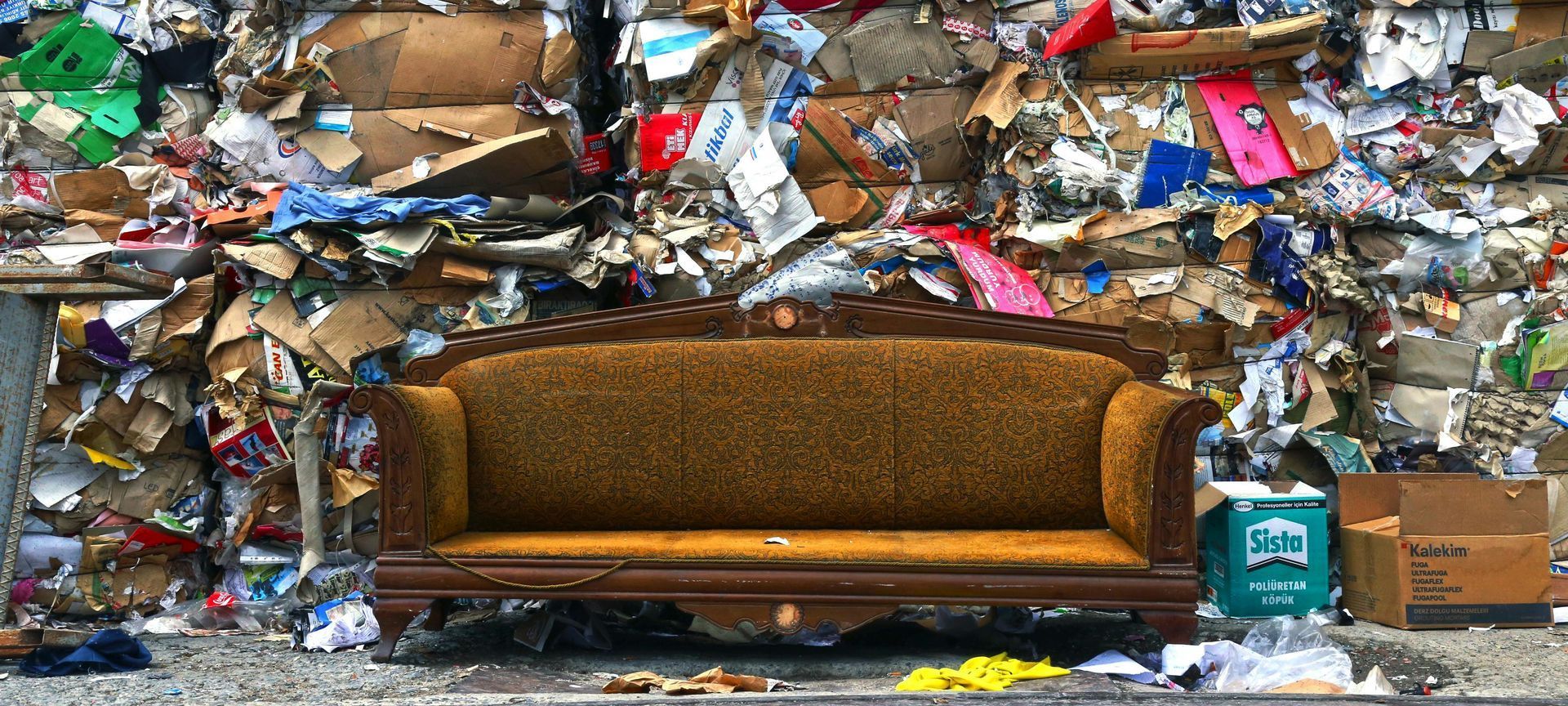 A couch is sitting in front of a pile of cardboard.