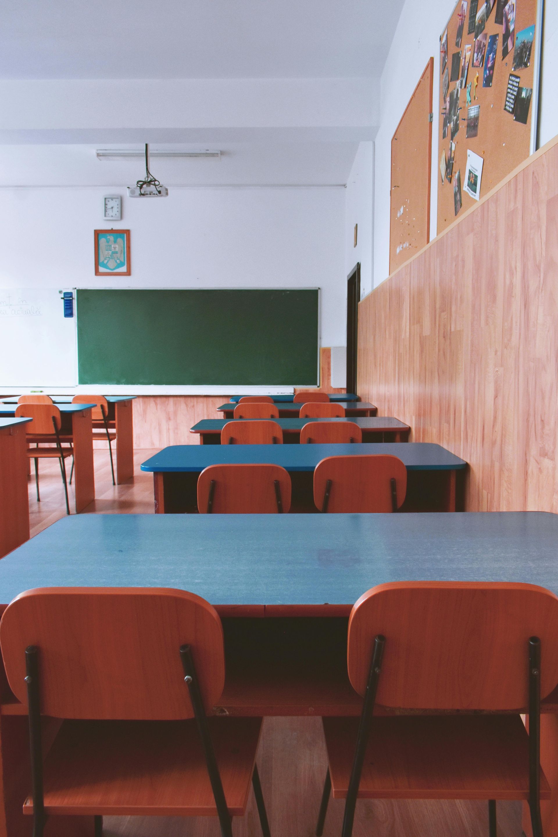 A classroom with tables and chairs and a green board