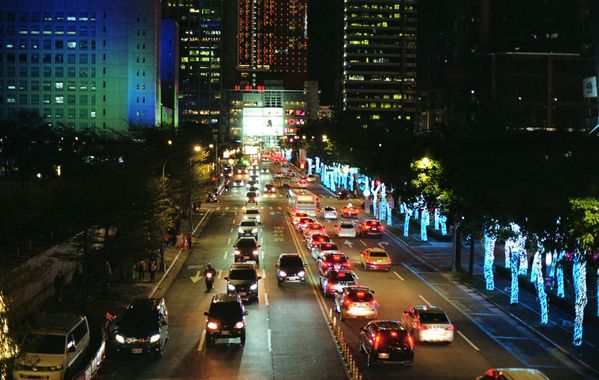 Nighttime city street with cars in traffic and blue-lit trees along the road