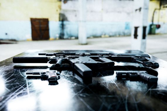 Several black handguns and a rifle laid out on a reflective table in a room