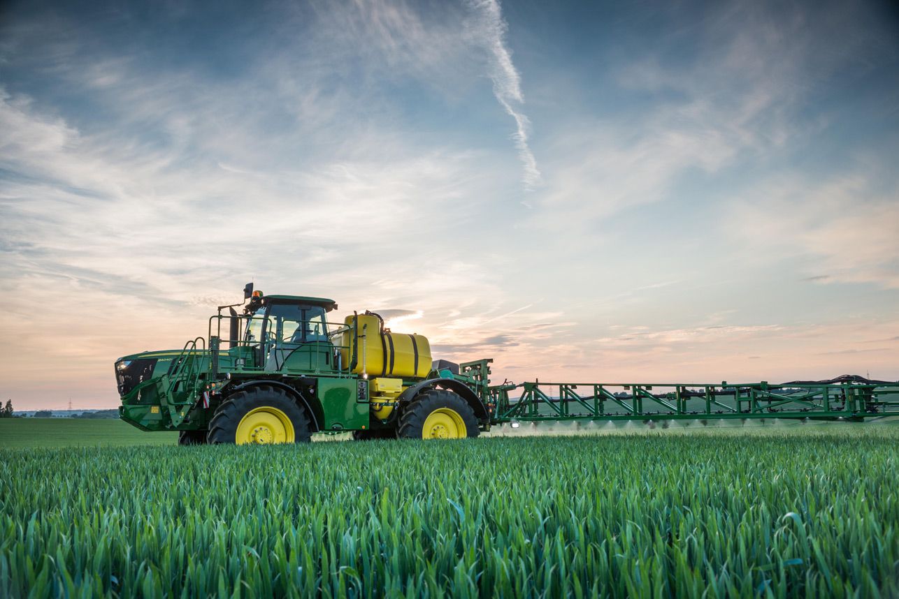 Green combine harvester working in a wheat field under a cloudy sky
